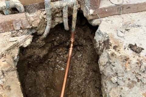 Hole dug in ground exposing pipe and leaky foundation